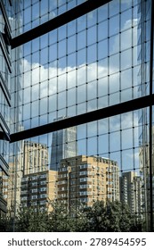 Modern glass facade with grid pattern reflects cityscape and sky. Urban architecture featuring contemporary building exterior with geometric window design and city views.