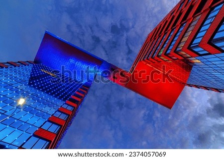Modern glass illuminated with blue and red color building (business center with offices) against cloudy dramatic sky in Novosibirsk city (Russia) at night.