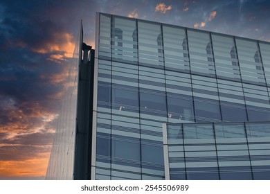 A modern glass and steel building against a colorful sunset sky. The building's facade features large windows and a grid pattern, while the sky is a blend of orange, purple, and blue. - Powered by Shutterstock