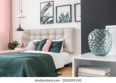 Modern, glass vase in a bedroom interior and a double bed in the background with wool blanket and colorful pillows - Shutterstock ID 1031095150
