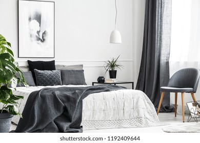 Modern, Gray Chair With Wooden Legs By A Window Of A Bright Bedroom Interior With A Dark Gray Blanket On A Comfy Bed