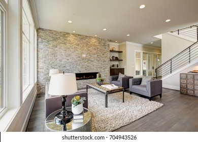 Modern great room features a floor to ceiling stone fireplace, gray tufted sofa paired with two gray armchairs over fluffy rug. Northwest, USA