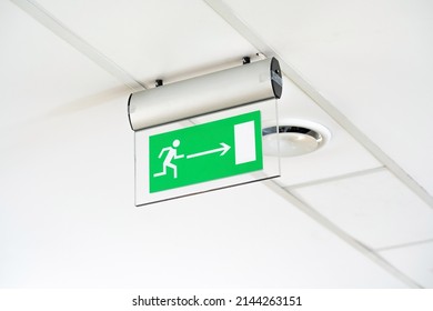 Modern Green Emergency Exit Route Door Arrow Sign On The Ceiling, Object Detail, Closeup, Nobody. Corporate Business Office Building Workplace Safety, Evacuation Plan, Brightly Lit Room, No People