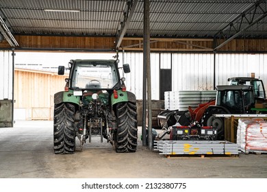 Modern green good-looking tractor stands in outside garage near agricultural fixtures and transport on farm or ranch on winter or summer cloudy day. Agriculture industry, cargo, bio production,  - Shutterstock ID 2132380775