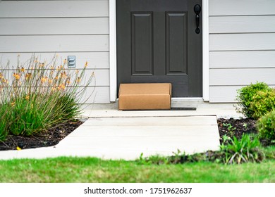 Modern Grey Front Door With Cardboard Box , Package Delivery Service Contact Less Delivery And Suburb Homes And Houses Front Porch With Modern Grey Front Door And Sidewalk With Green Shrubs And Grass