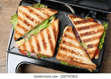 Modern grill maker with sandwiches on wooden table, top view