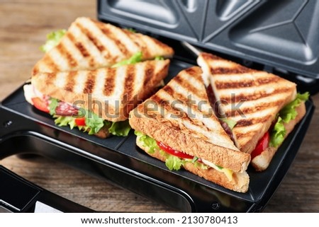 Modern grill maker with sandwiches on wooden table, closeup
