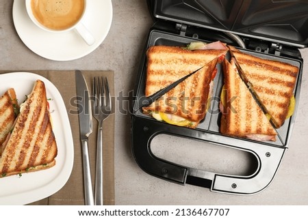 Modern grill maker with tasty sandwiches on light grey table, flat lay