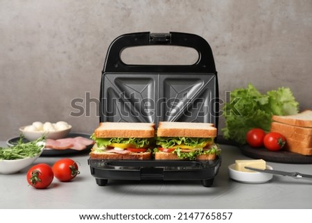 Modern grill maker with tasty sandwiches on light grey table
