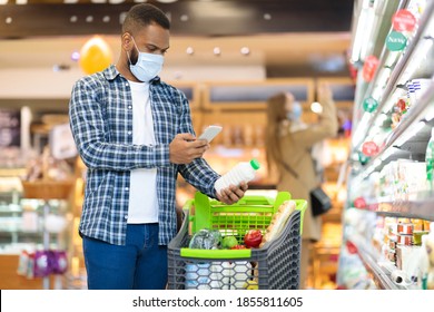 Modern Grocery Shopping. African American Man Using Mobile Phone Scanning Product With Smartphone App Standing With Trolley In Supermarket. Groceries Checklist Application. Free Space For Text