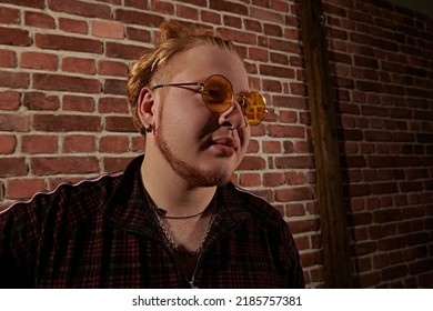 A Modern Guy With Red Hair And Short Beard Wearing A Casual Sports Suit And Stylish Glasses Stands In A Loft Style Room. Youth Culture. Hip-hop Fashion. Men's Youth Style.