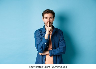 Modern Guy Shushing At Camera, Press Finger To Lips And Telling A Secret, Making Taboo Sign, Standing On Blue Background