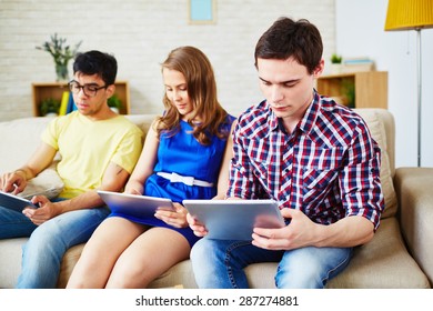 Modern guys and girl sitting on sofa with touchpads