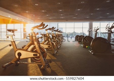 Modern gym interior with equipment. Fitness club with training exercise bikes, backlight in evening sunlight.