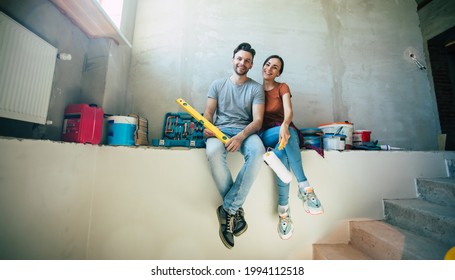 Modern Happy Young Couple In Love In Casual Clothes During New Home Repair Or Renovation Of Walls With A Lot Of Tools For This