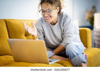 Modern happy young woman smile and have fun in video call computer online activity. Calling friends using internet and laptop connection. Smart female people sitting on yellow sofa with notebook pc
