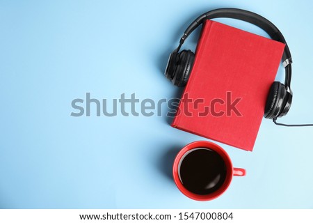 Modern headphones with hardcover book and coffee on light blue background, top view. Space for text