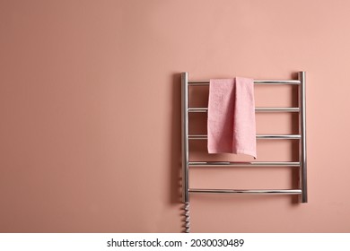 Modern Heated Towel Rail With Warm Soft Towel On Light Pink Wall. Space For Text