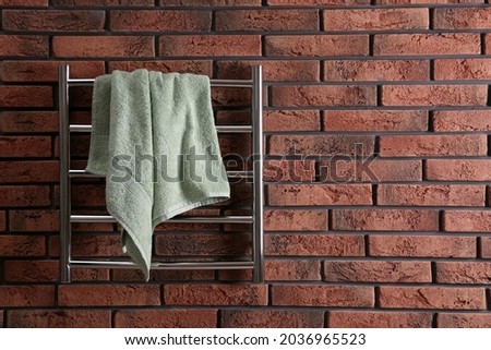 Modern heated towel rail with warm soft towel on red brick wall. Space for text