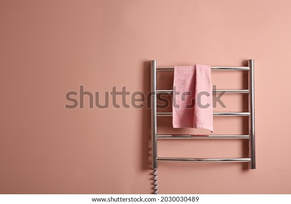 Modern heated towel rail with warm soft towel on\
light pink wall. Space for\
text