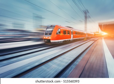 Modern High Speed Red Passenger Commuter Train In Motion At The Railway Platform At Sunset. Railway Station. Railroad With Motion Blur Effect. Industrial Landscape With Train. Vintage Toning