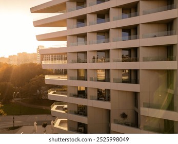 Modern high-rise building at sunset, featuring glass balconies and a tranquil urban setting. The golden hour lighting adds warmth to the minimalistic architecture. Shot with a drone - Powered by Shutterstock