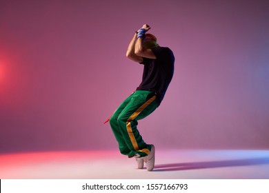 Modern hip hop dancer frozen in movie, standing on tiptoe, covering head with hands, expressing dance element, practicing in dance studio, full of energy break dancer