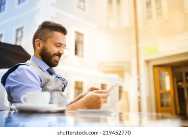 Modern hipster businessman drinking espresso coffee in the city cafe during lunch time and using mobile phone