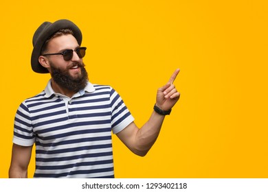 Modern hipster man in hat and sunglasses showing direction with finger on yellow background - Shutterstock ID 1293402118