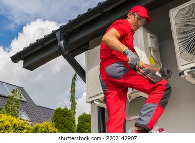 Modern Home Heating Technologies. Professional Caucasian HVAC Worker In His 40s Maintain Heat Pump Repair From A Ladder.