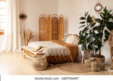 Modern home interior design. White and beige blankets on comfortable bed in boho bedroom interior  scandinavian style.Textured walls, wooden floor, sunny shades, natural materials, straw screen
