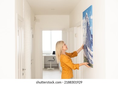 Modern Home Interior And Domestic Decor. Smiling Young Woman Hanging Painting, Putting Photo Picture Frame On The Wall. Casual Lady Taking Care Of Coziness In Her New Stylish Apartment, Profile