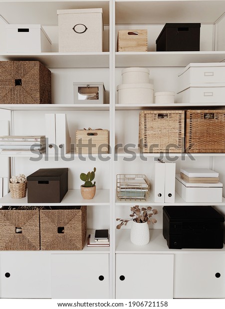 Modern home office cabinet interior\
design concept. White storage shelves rack with rattan boxes,\
cactus, vases, decorations. Neutral beige and white\
concept.
