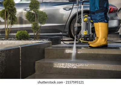 Modern Homeowner Washing His Garden Paths And Driveway Using Powerful Pressure Washer Next To His Car. Home Surroundings Maintenance.