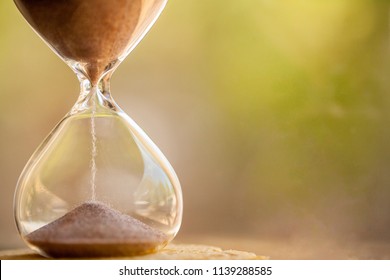 Modern Hourglass With Green Background -- Sand Trickling Through The Bulbs Of A Crystal Sand Glass. Every Second Counts. Symbol Of Time. Countdown.