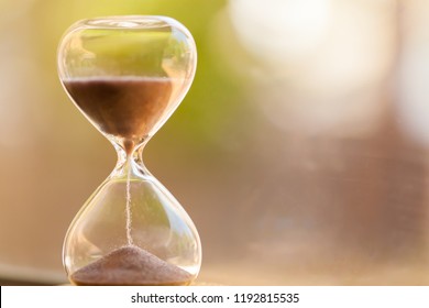 Modern Hourglass with green background -- sand trickling through the bulbs of a crystal sand glass. every second counts. symbol of time. countdown. - Shutterstock ID 1192815535