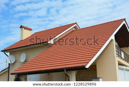 Modern house with chimney, red clay tiled roof, rain gutter and gable and valley type of roof construction. Roofing Construction.