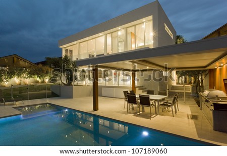 Modern house at dusk with swimming pool and barbecue in backyard 