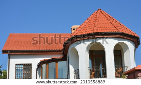 A modern house with terracotta clay, ceramic tiled roof, circle open arched balcony with wrought iron railing and radius, curved roof gutter system. 