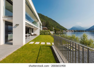 Modern house of two apartments with a beautiful garden directly on Lake Ceresio. Sunny day with blue sky. Minimalist and linear architecture. Panoramic view of the lake. Space for your text