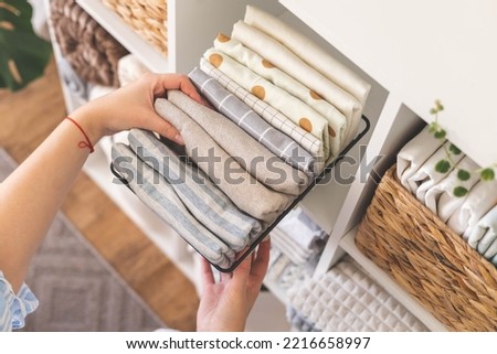 Modern housewife putting neatly folded towels, pillowcases, duvet covers into plastic metallic case boxes use vertical method storage organization. Woman making seasonal tidying up at home cupboard