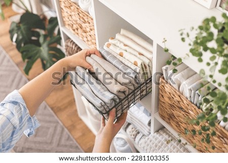 Modern housewife putting neatly folded towels, pillowcases, duvet covers into plastic metallic case boxes use vertical method storage organization. Woman making seasonal tidying up at home cupboard