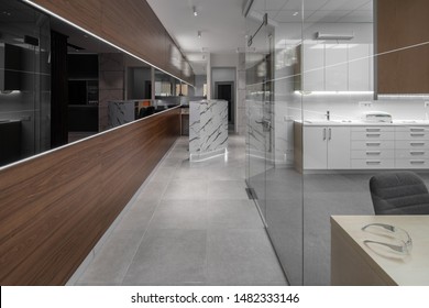 Modern Illuminated Interior Of A Dental Clinic With Light And Textured Brown Walls And Tiled Gray Floor. There Is A Reception Desk, Doors, Cabinet With Glass Partition, Table, Lockers With A Sink.