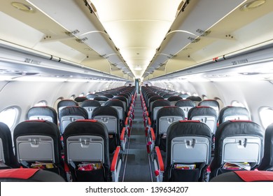 Modern Interior Of Aircraft. Black And Red Seats Inside Airplane. Symmetric Vanishing Row Of Seats Inside Air Transport. Economy Class Of Flight. Equipment For Travelling. Empty Illuminated Plane.