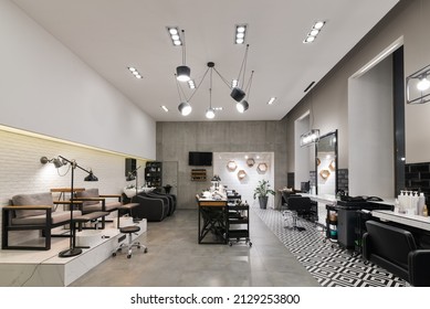 Modern interior of the beauty salon which consist of nail salon and barbershop with black lamps and concrete wall. Mirrors, chairs, backwashes and other equipment are in the salon. - Shutterstock ID 2129253800