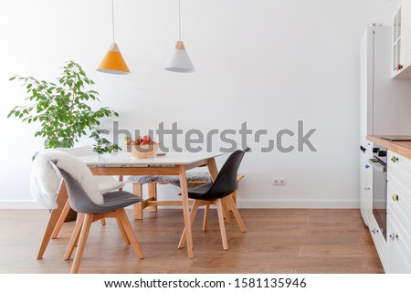 Modern interior of cozy kitchen, dining room, white furniture, lamps above wooden table, chairs, apples, bowl. Concept decor, design, advert, credit, mortgage, home for young family, magazine cover