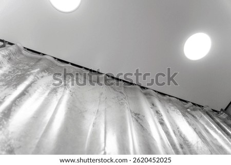 Modern interior design featuring elegant silver curtains hanging from a ceiling-mounted rail, with spotlights providing soft illumination, creating a stylish and contemporary ambiance
