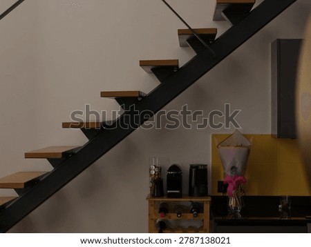 Modern interior design featuring an open metal and wood staircase against a white wall with a small kitchen counter and coffee station underneath