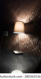 Modern interior desk lamp casting warm light shadows on textured wall