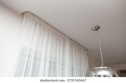 A modern interior element: lightweight, translucent curtains (tulle) attached to a hidden rod in a recess in a stretch ceiling. A chrome chandelier is visible nearby.